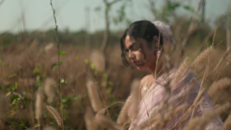 woman in pink dress contemplating in dry grass field, soft focus, warm daylight