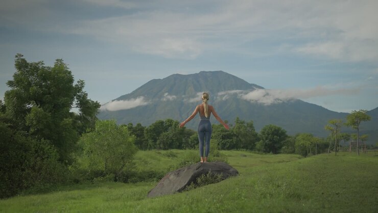 Donna spirituale che pratica yoga sale su un masso alzando le braccia nella posizione del saluto al sole verso il monte Agung