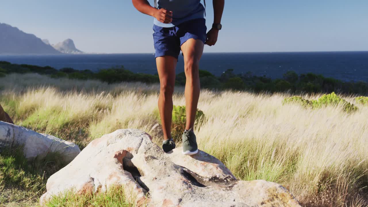 hombre afroamericano haciendo ejercicio al aire libre saltando sobre una roca en el campo en una montaña