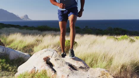 Hombre-Afroamericano-Haciendo-Ejercicio-Al-Aire-Libre-Saltando-Sobre-Una-Roca-En-El-Campo-En-Una-Montaña