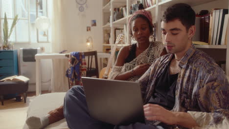 young man using laptop and talking with girlfriend in bedroom