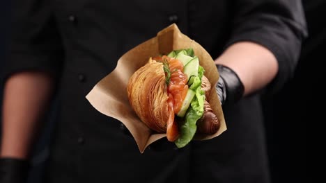 chef holding a delicious smoked salmon croissant sandwich