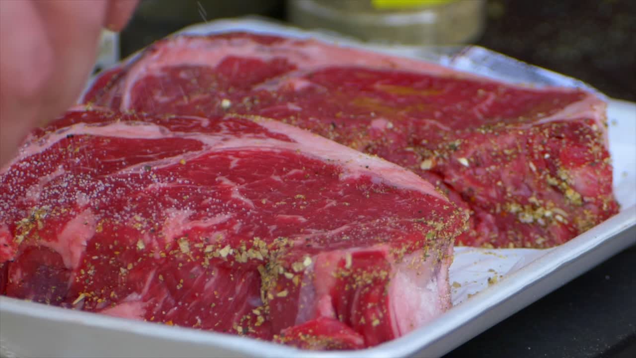 A hand pours salt all over a rib eye steak in slow motion