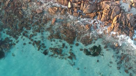 Aerial-drone-topdown-moving-away-from-the-ocean-with-crystal-clear-calm-turquoise-water-in-castle-rock-Western-Australia