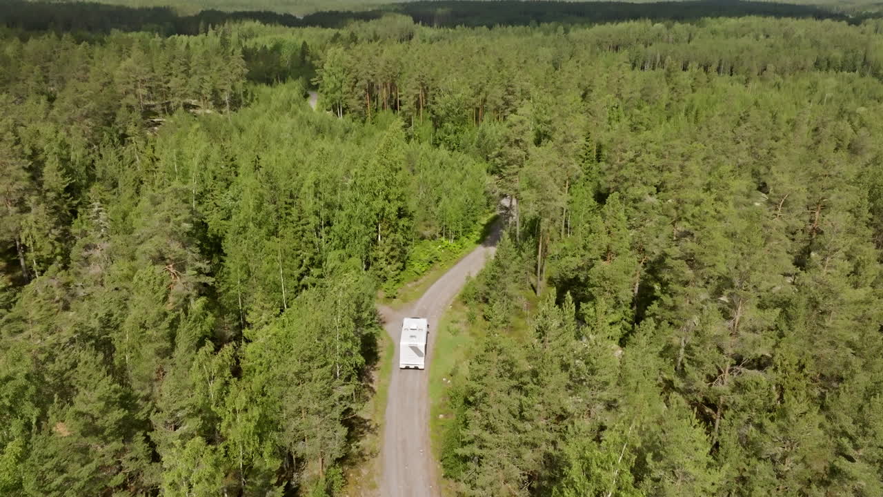 Aerial tilt shot tracking a RV from behind, driving on a dirt road in a forest