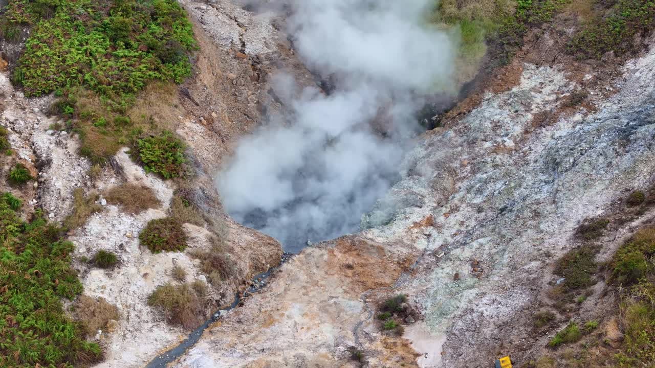 Aerial footage of a steaming volcanic sulfur crater with visible gas vents and mineral deposits, showcasing geothermal activity in nature. Sikidang Crater, Dieng, Indonesia