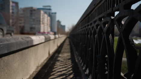 close view of an urban road with two moving vehicles in the background, it focus is on the road barrier with shadows cast by the railing