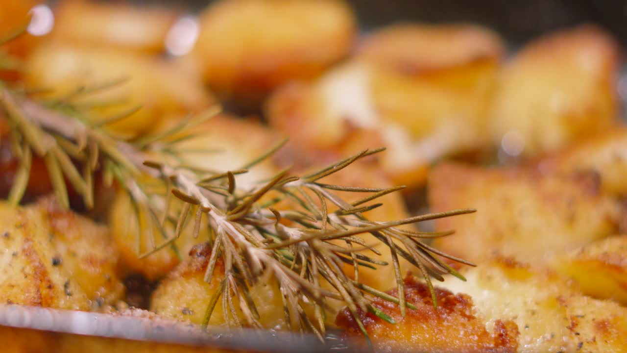 Crispy Roast Potatoes Sitting in Bubbling Oil Fresh Out the Oven with Rosemary Resting on Top for Flavour as Camera Pans Around in Slow Motion. Kitchen Cooking Footage 4K.