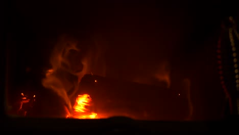fuego de leña en casa en cámara lenta que quema madera con llama naranja y brasas calientes con fondo oscuro, primer plano llamas parpadeantes