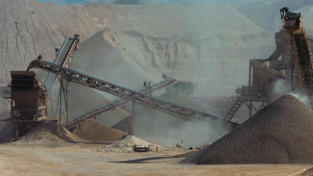 Industrial sand mining - 2 clips, long shot Stone crusher (rock stone crushing machines) belt is rolling and dropping off gravels on a pile of gravels.