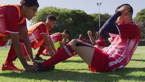 video of diverse group of male football players warming up on field, doing sit-ups