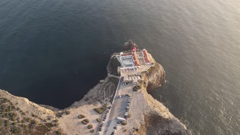 Aerial-pull-out-view-of-Saint-Vincent-cape-lighthouse-located-on-top-of-natural-formation-rugged-cliff,-Sagres