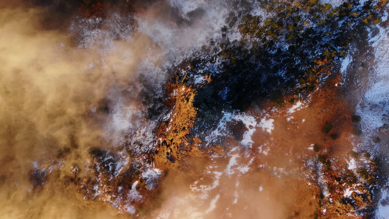 Drone aéreo inclinándose hacia arriba con montañas nevadas y un paisaje de nubes al amanecer dorado en invierno
