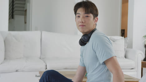 portrait of happy asian male teenager wearing headphones in living room