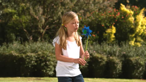 little girl blowing a pinwheel in her garden