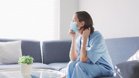 caucasian female doctor wearing face mask at home sitting on couch