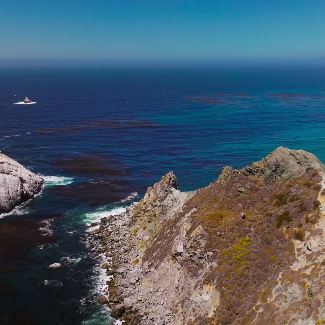Sharp spiky rocks with some lichen growing on. Beautiful scenery of the blue sea water with algae on surface. Hazy horizon at backdrop