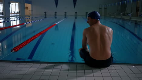 male swimmer sitting at the edge of an indoor swimming pool
