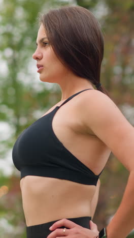 girl outdoor in black singlet standing and breathing in deeply with hand on waist, calm and focused expression, healthy posture, feeling refreshed, natural beauty, fitness moment, outdoor breath