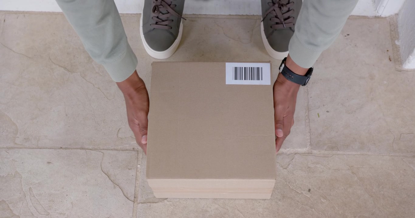 African American man spotting parcel with barcode, stepping on tiled doorstep, reaching and lifting