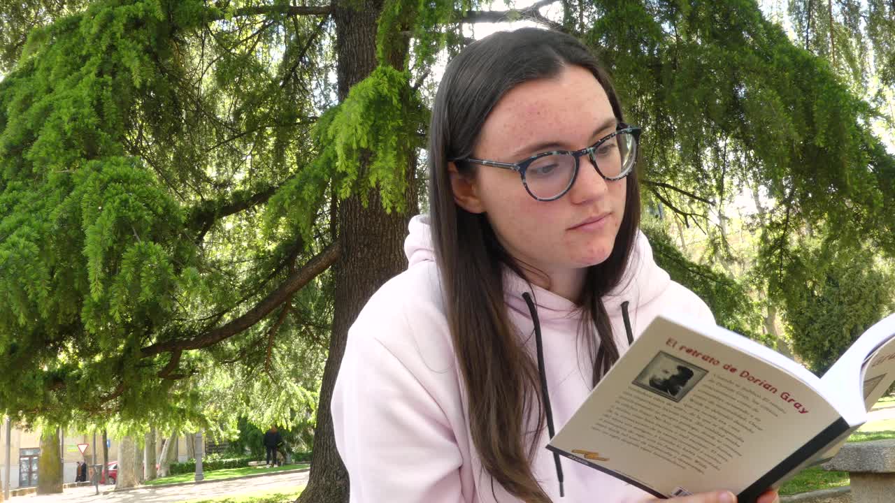 estudiante leyendo una novela junto a un árbol en un parque, video al aire libre