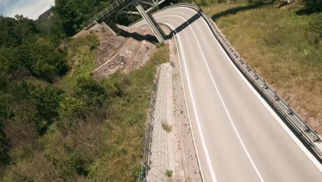 dynamic flying with fpv racing drone along a winding road and under and above an old railway bridge passing by a red van and other cars