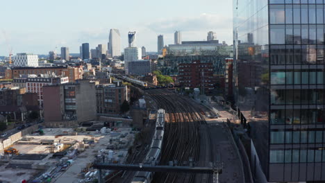 Forwards-tracking-train-unit-driving-through-urban-district,-passing-by-another-train.-Elephant-and-Castle-skyscrapers-in-background.-London,-UK