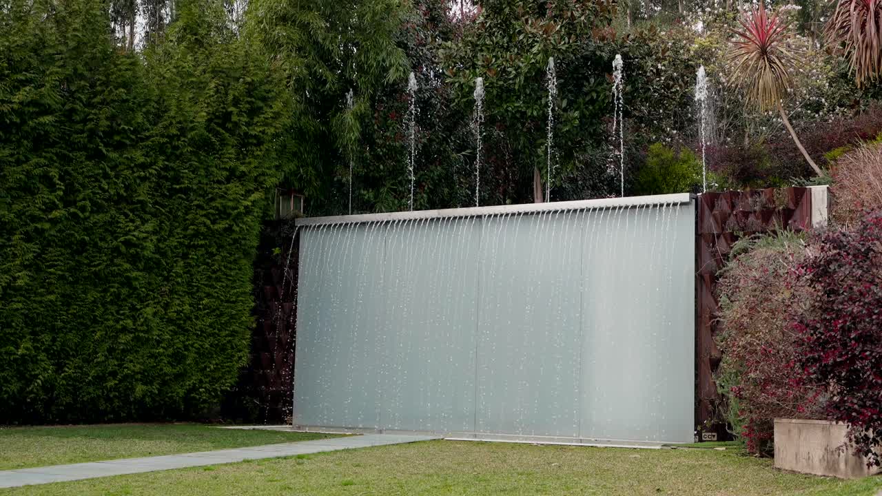 Water flows from a sleek vertical fountain in landscaped garden with foliage