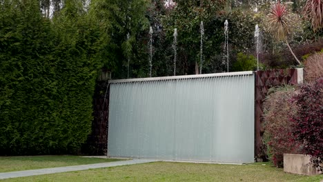 water flows from a sleek vertical fountain in landscaped garden with foliage
