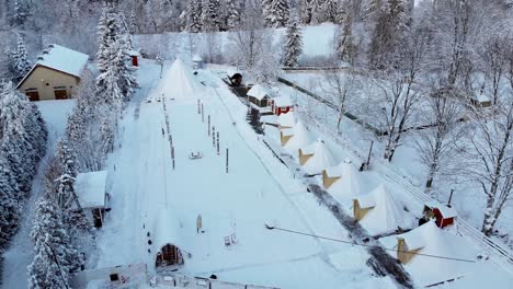 aerial view towards cottages, sauna and a big tent in a finnish holiday resort village, in middle of polar forest, on a cloudy, winter day - circling, drone shot