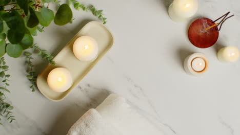 Overhead-View-Looking-Down-On-Still-Life-Of-Lit-Candles-And-Incense-Stick-With-Green-Plant-And-Soft-Towels-As-Part-Of-Relaxing-Spa-Day-Decor