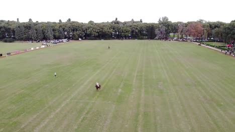 a polo player strikes a ball during warm-up on a polo field, preparing for the match on a cloudy day.