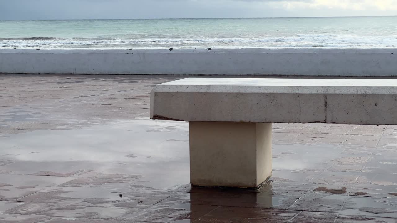 close de uma calçada molhada ao lado de um banco de pedra