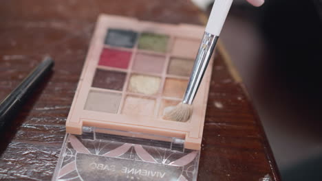 close-up view of makeup palette with contour powder in various colors, including shades of brown, pink, and red, focus on brush tapping powder in cosmetics kit, makeup and beauty products