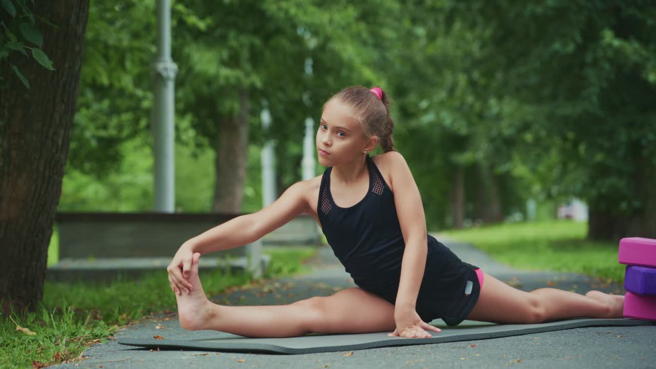 A young girl practicing her stretching routine outdoors, showcasing flexibility and control while engaged in yoga and fitness on a summer day