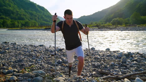 인공 다리 를 가진 사람 이 산 에 있는 강 을 따라 산책 하고 있다