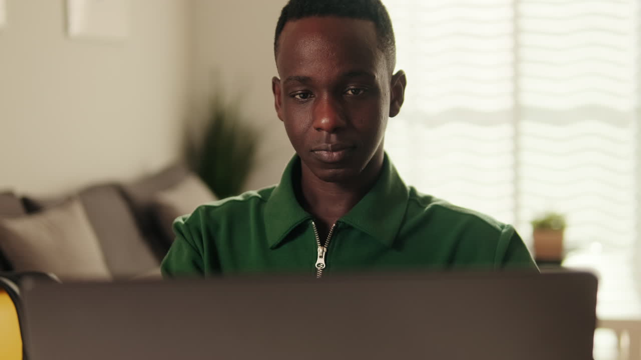 Junger afroamerikanischer Mann arbeitet lächelnd am Laptop.
