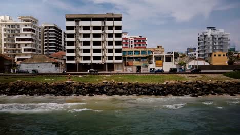 drone flying right along ocean coast street in colombo sri lanka. aerial tracking shot of traffic vehicles and buildings
