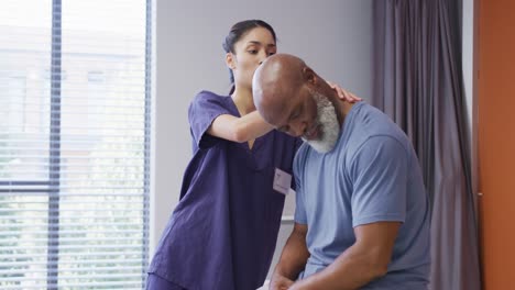 Diverse-female-physiotherapist-and-senior-male-patient-in-hospital-physical-therapy-session-on-neck