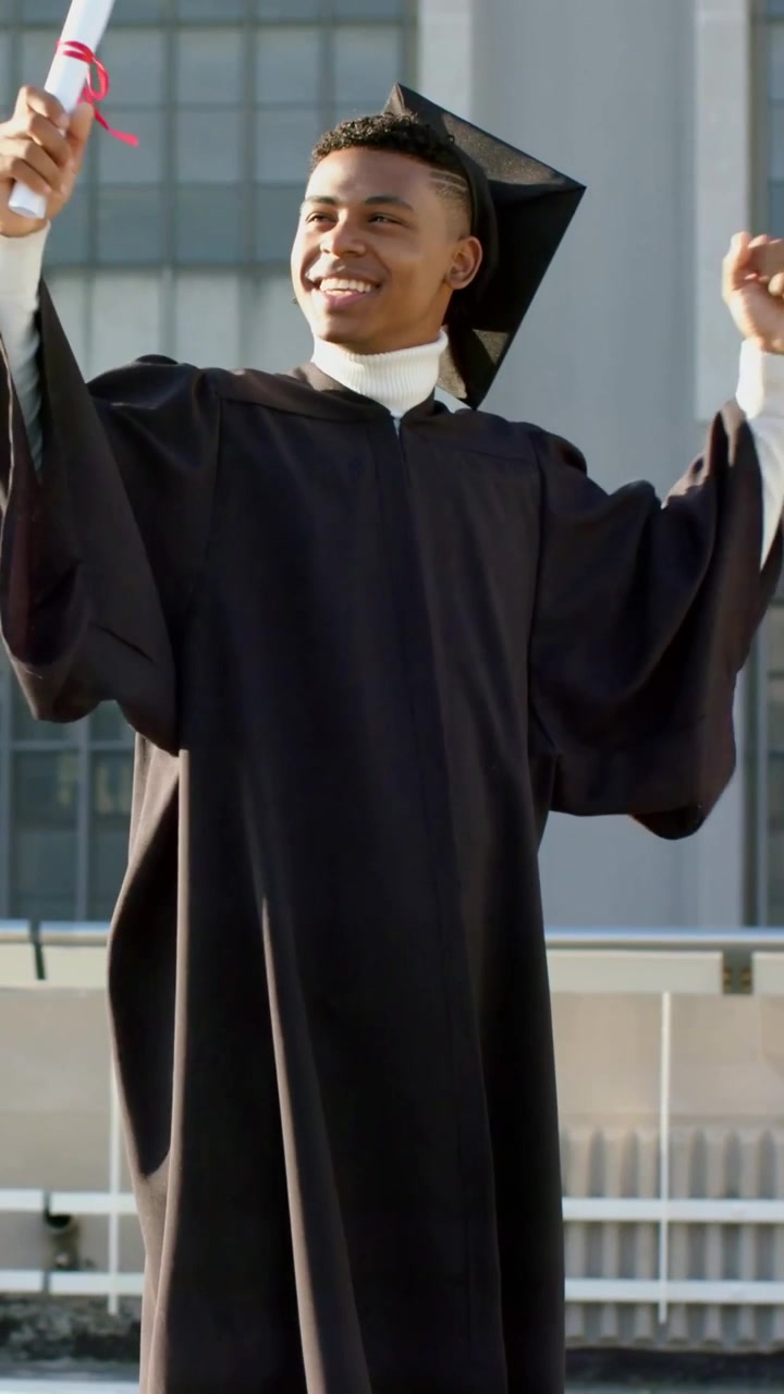 Video verticale: Sollevamento di un diploma di laurea, uomo con tocco che alza le braccia su un tetto, sciogliendo un nastro rosso.