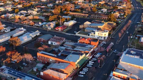 drone camera glides above coonabarabran’s main street, capturing historic buildings, rooftops, and warm sunset light in a smooth, descending motion