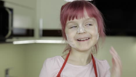 Little-child-girl-in-the-kitchen-dressed-in-apron-and-scarf.-Face-in-flour