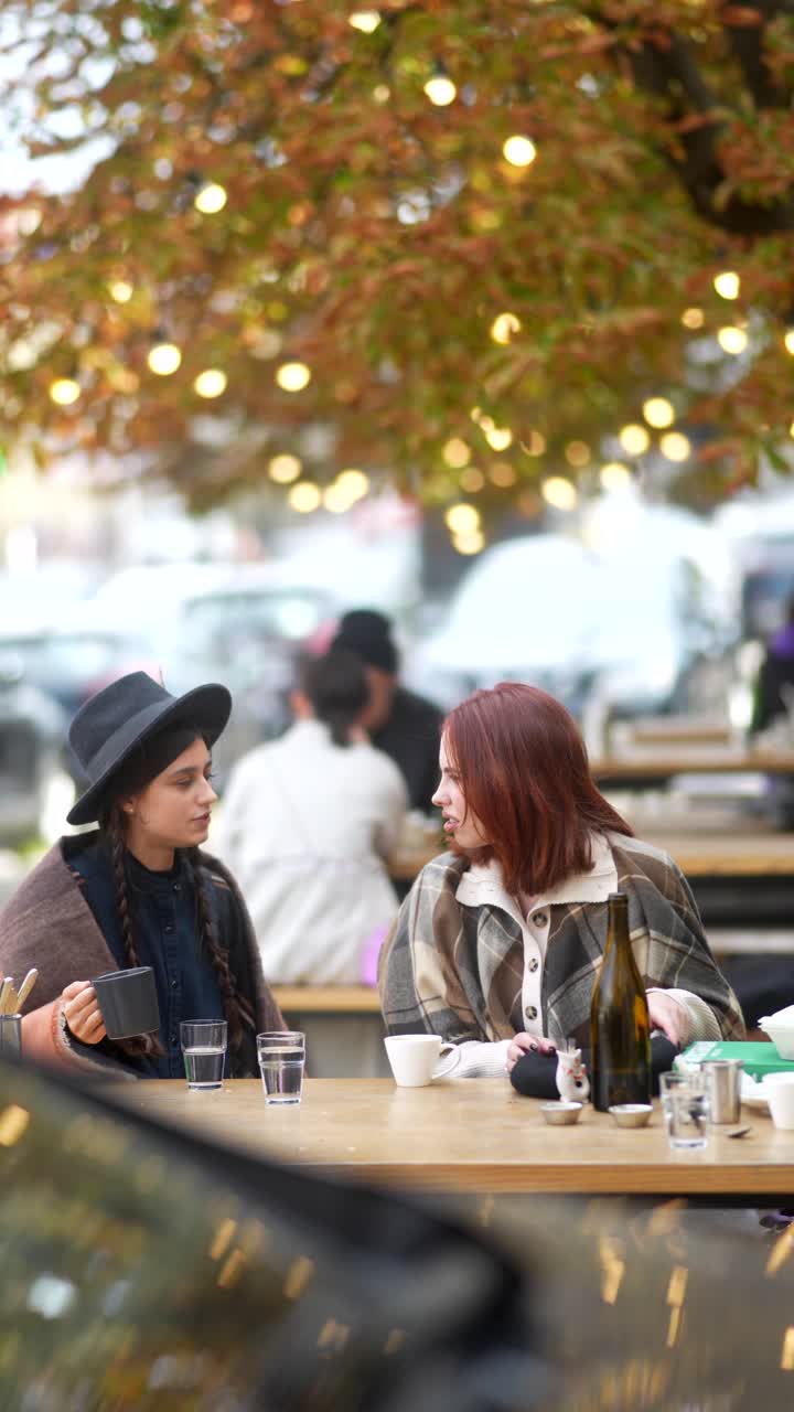 두 여인이 야외 카페에서 대화를 나누고 있다