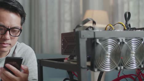 close up of asian man wearing glasses using smartphone and mining rig for mining cryptocurrency