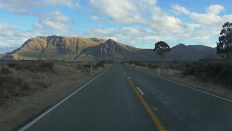 a car traveling fast heading to a beautiful mountainous landscape in new zealand on a fine sunny weather - medium shot