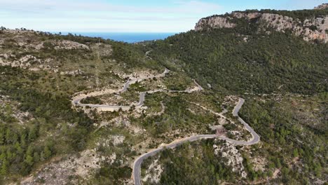 aerial view showing serpentine road on green hill of esporles on mallorca and ocean in background