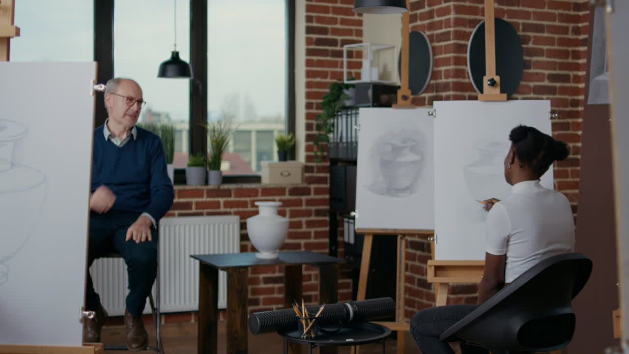 Senior man teaching people in art class to draw on canvas