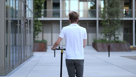 back view of a young businessman walking with an e-scooter medium shot