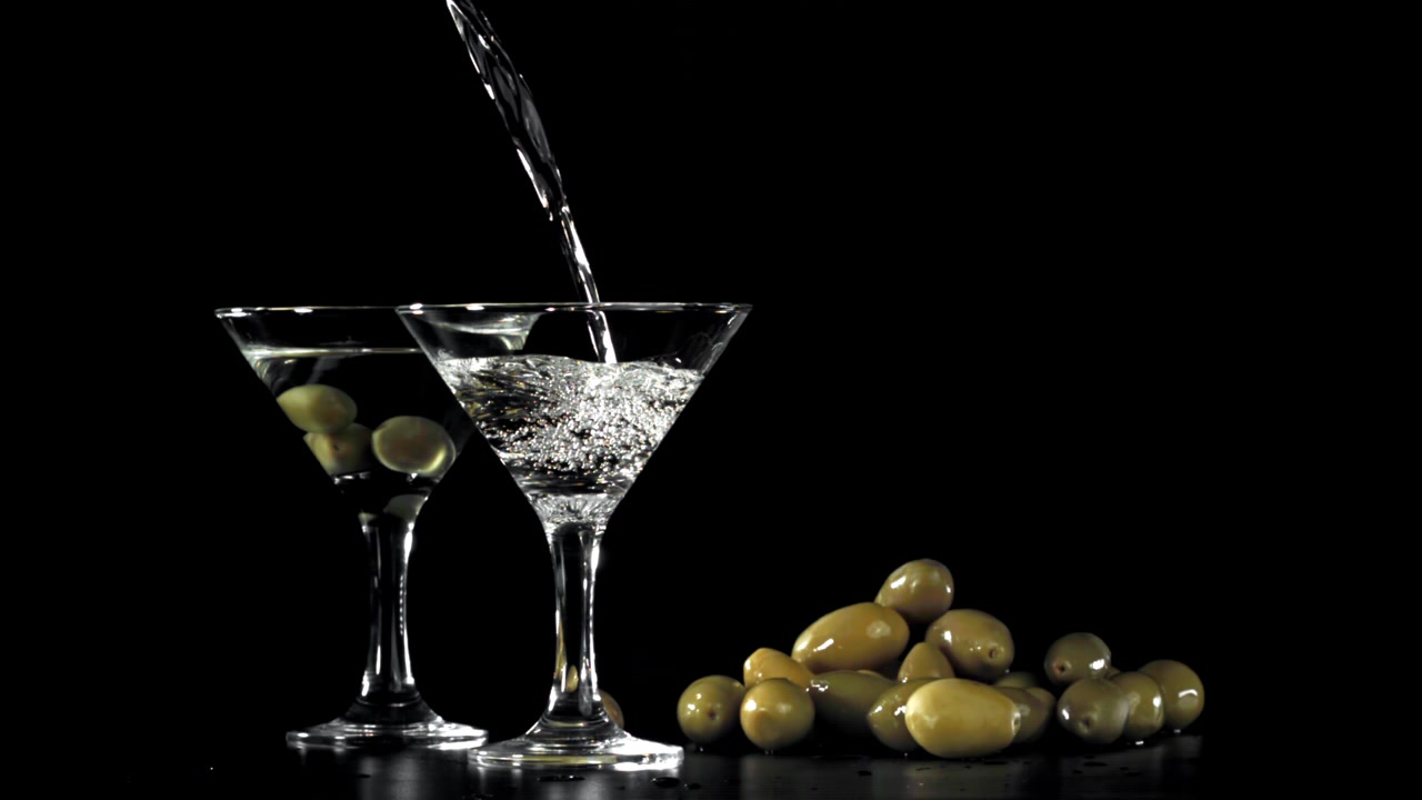 Martini versato in un bicchiere con olive su sfondo nero