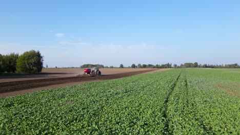 aerial flying towards tractor with harrow system plowing ground on cultivated farm field, pillar of dust trails behind, preparing soil for planting new crop, agriculture concept, pov